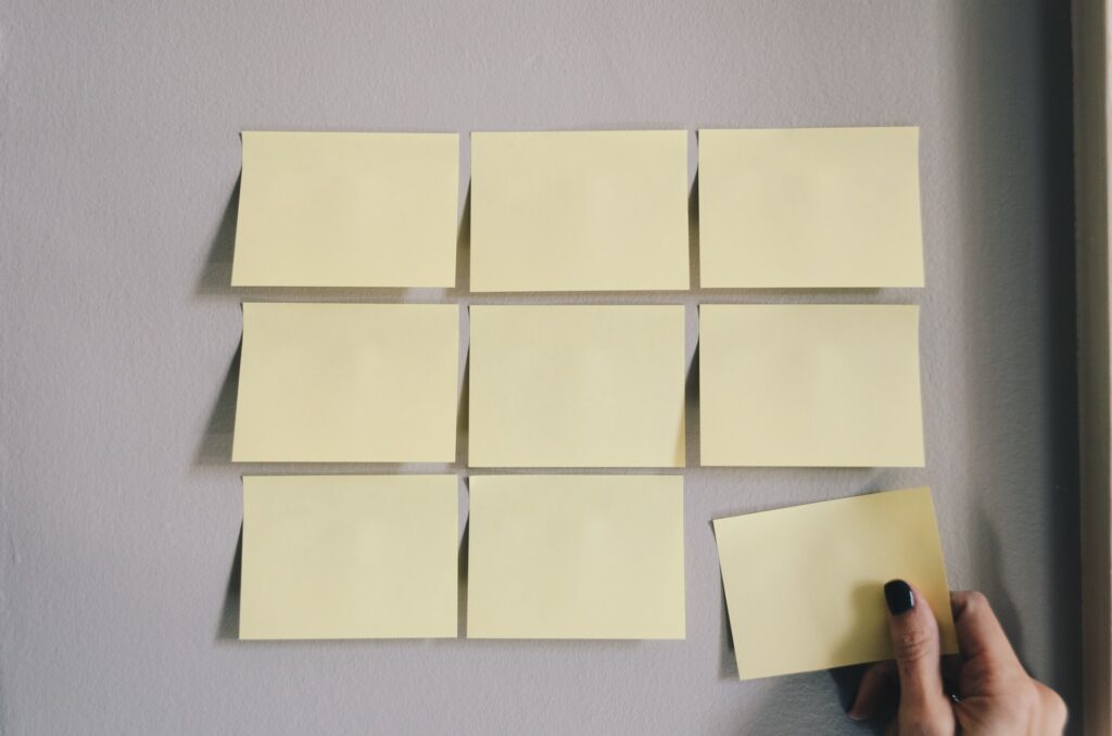 A hand adds a sticky note to a group of sticky notes on a wall.